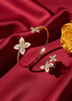 Set SIA Floral Embrace, brățară și inel aurii cu design floral și cristale strălucitoare pe fundal de mătase roșie