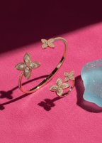 Set SIA Floral Embrace, brățară și inel aurii cu design floral și cristale pe fundal roz elegant