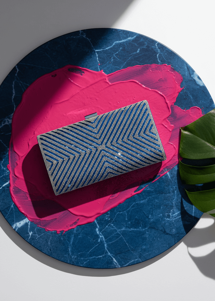 Clutch Sapphire Shine plic elegant cu cristale albastre și model geometric, expus pe fundal albastru cu accente roz