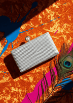 Clutch Crystal Pearl argintiu cu cristale și închizătoare perlă, pe fundal portocaliu vibrant cu pană de păun