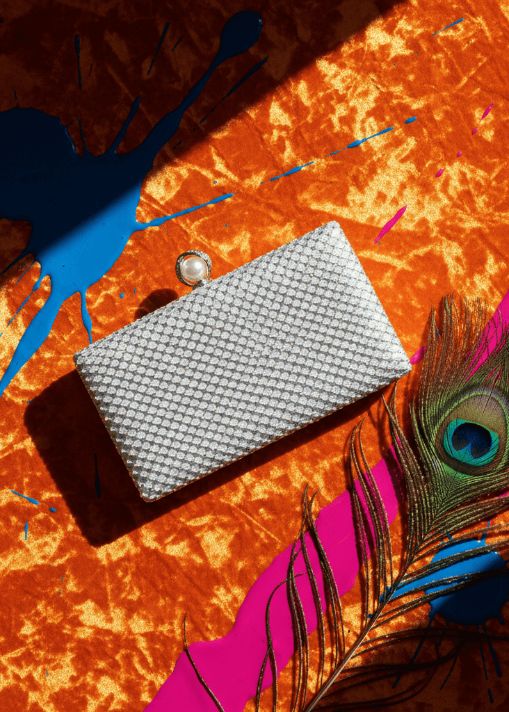 Clutch Crystal Pearl argintiu cu cristale și închizătoare perlă, pe fundal portocaliu vibrant cu pană de păun