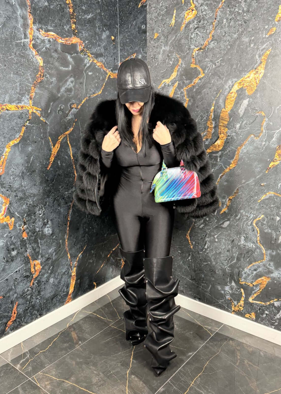 Femeie în Sia Salopeta modelatoare Venom, outfit negru elegant, pardesiu din blană și geantă colorată, ținută modernă cu atitudine.