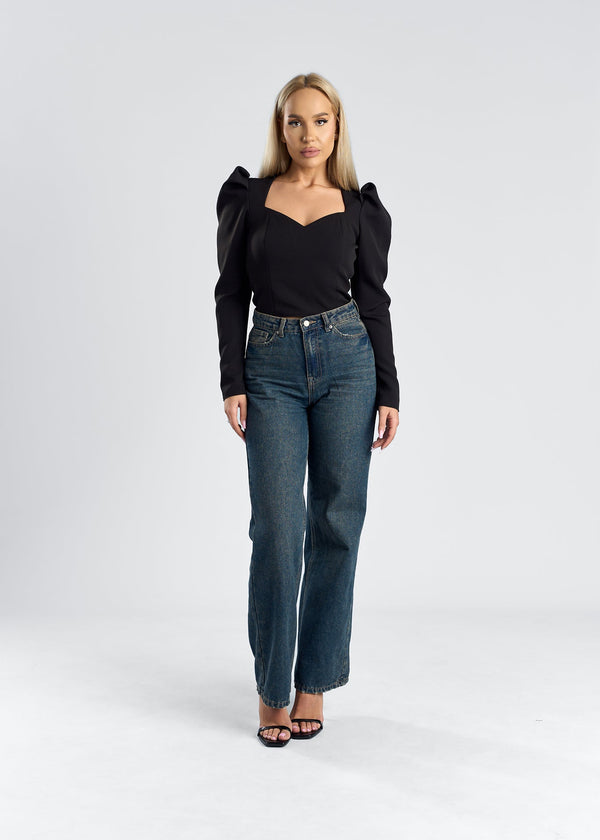 Top cu umeri supradimensionați și decolteu elegant, purtat de o femeie cu jeans în imagine.