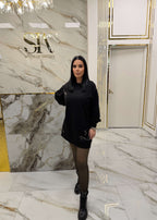 Femeie purtând un hoodie "ATTITUDE" tip rochie cu ace metalice, pozată într-un decor luxos cu marmură albă și detalii aurii.