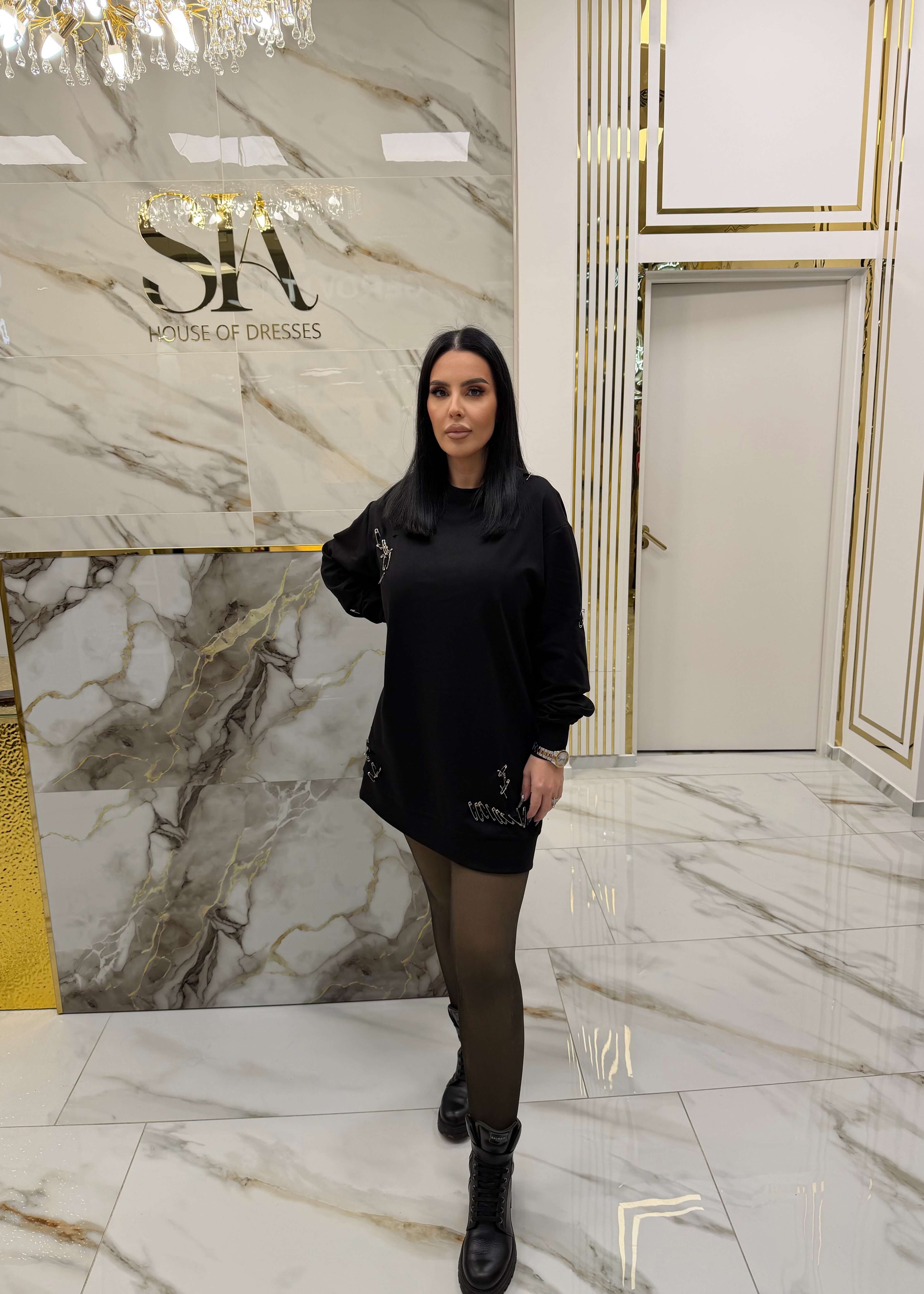 Femeie purtând un hoodie "ATTITUDE" tip rochie cu ace metalice, pozată într-un decor luxos cu marmură albă și detalii aurii.