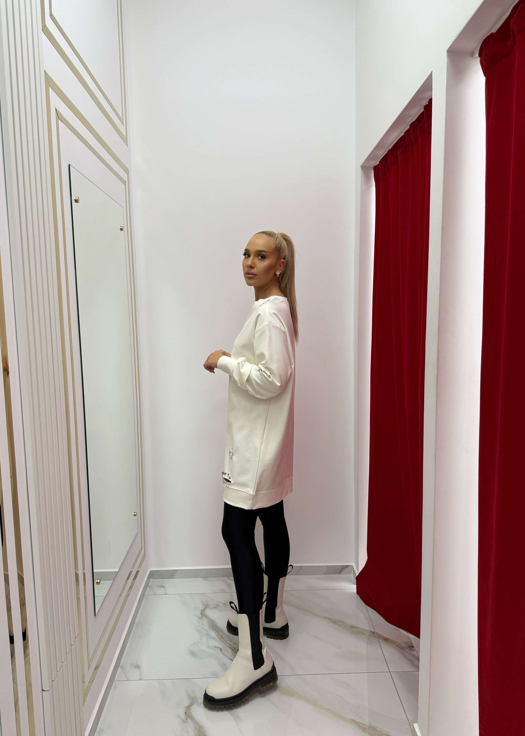 Persoană purtând SIA "ATTITUDE" hoodie în rochie cu ace metalice, stil urban, culoare albă, în fața unei draperii roșii.