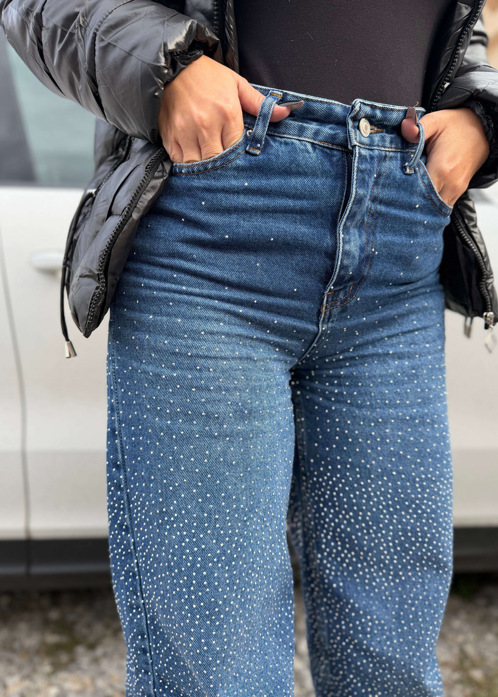 Blugi talie înaltă cu cristale, ușor evazați CRYSTAL DENIM purtați cu geacă neagră, detaliu close-up pe pietre strălucitoare