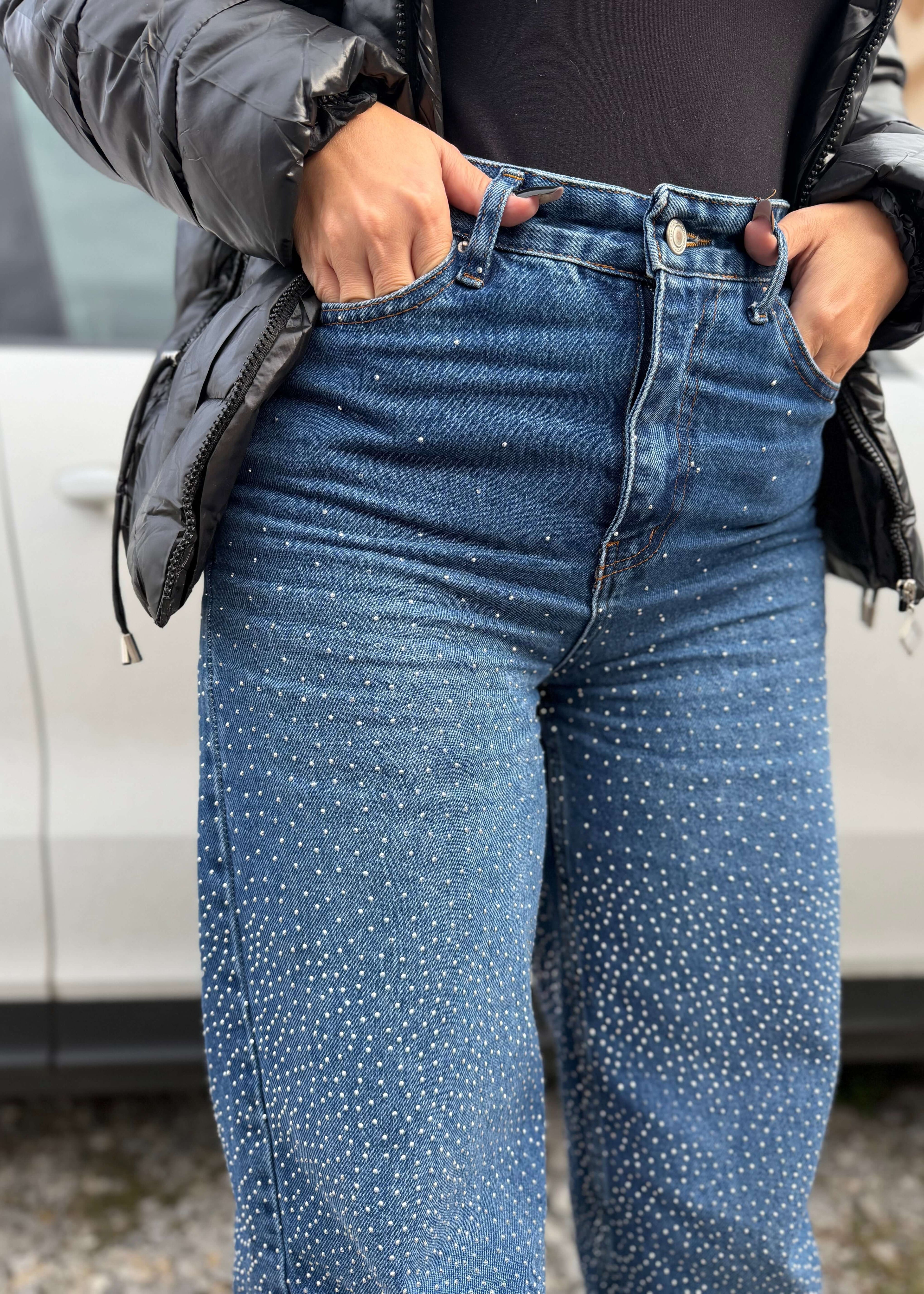 Blugi talie înaltă cu cristale, ușor evazați CRYSTAL DENIM purtați cu geacă neagră, detaliu close-up pe pietre strălucitoare