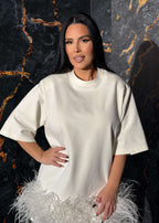 Tricou tip rochie cu pene statement "Feather Love", minimalist și extravagant, pe un model în fața unui perete texturat.