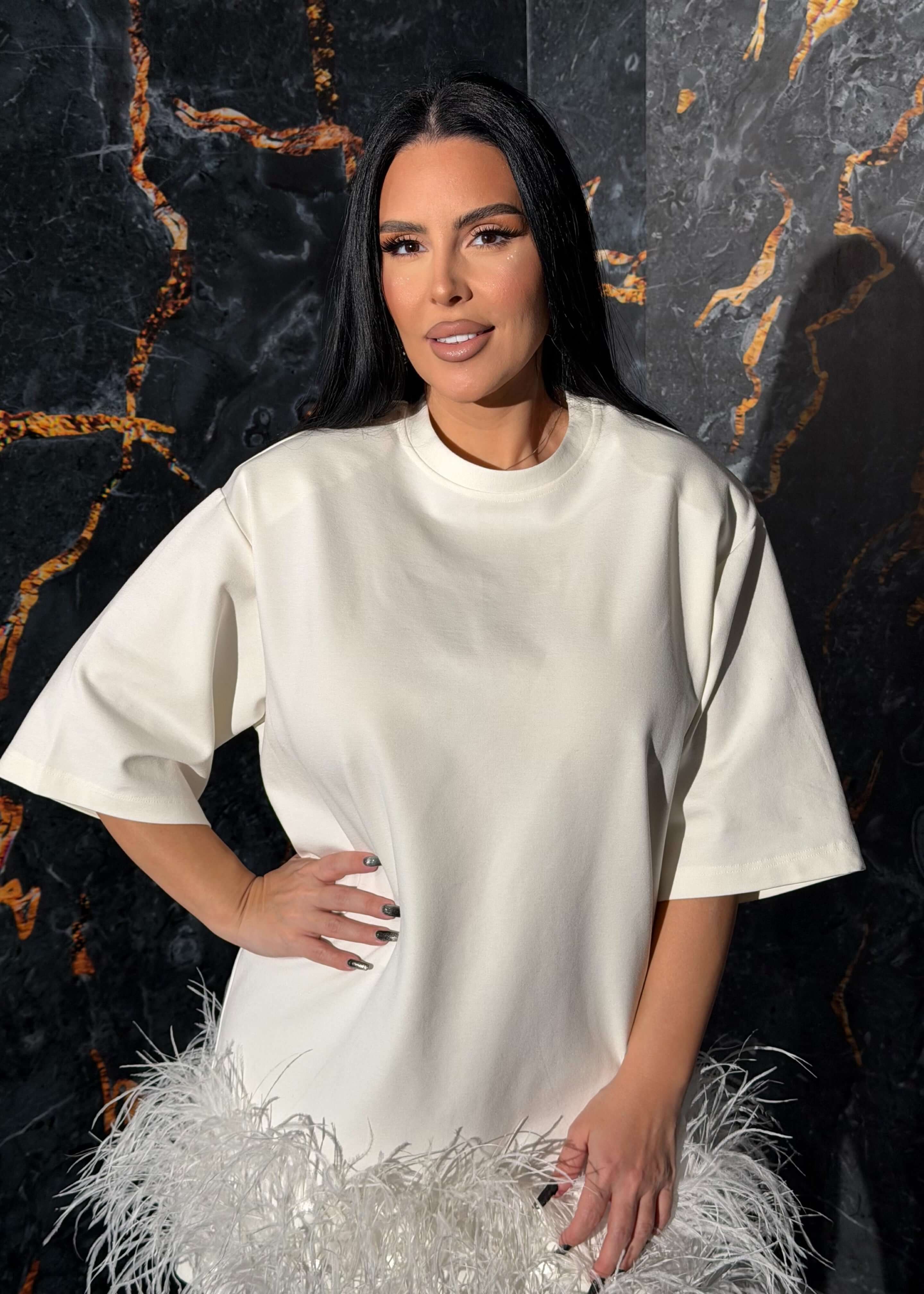 Tricou tip rochie cu pene statement "Feather Love", minimalist și extravagant, pe un model în fața unui perete texturat.