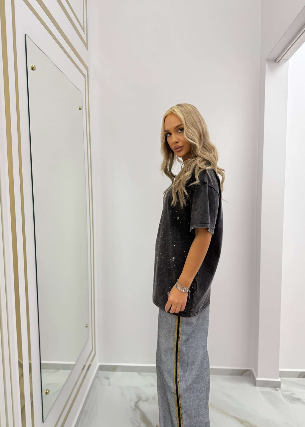 Tricou oversized SIA "RELIGION" cu efect washed și accente strălucitoare, purtat cu pantaloni gri cu dungi laterale aurii