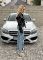 Blugi cu capse laterale SNAP ME, purtați cu geacă de piele neagră și pantofi bej, stil urban casual în fața unei mașini