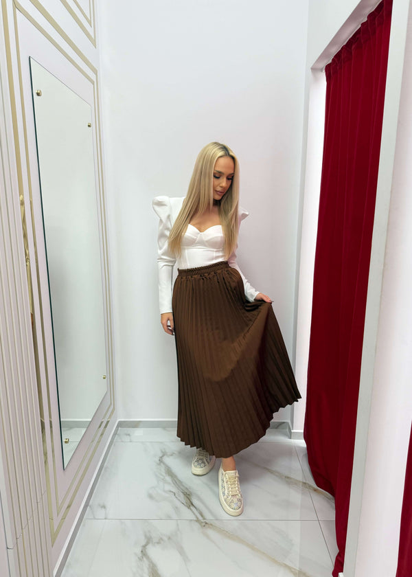 Model purtând Fustă midi plisată maro, design urban și modern, într-o cabină de probă elegantă.