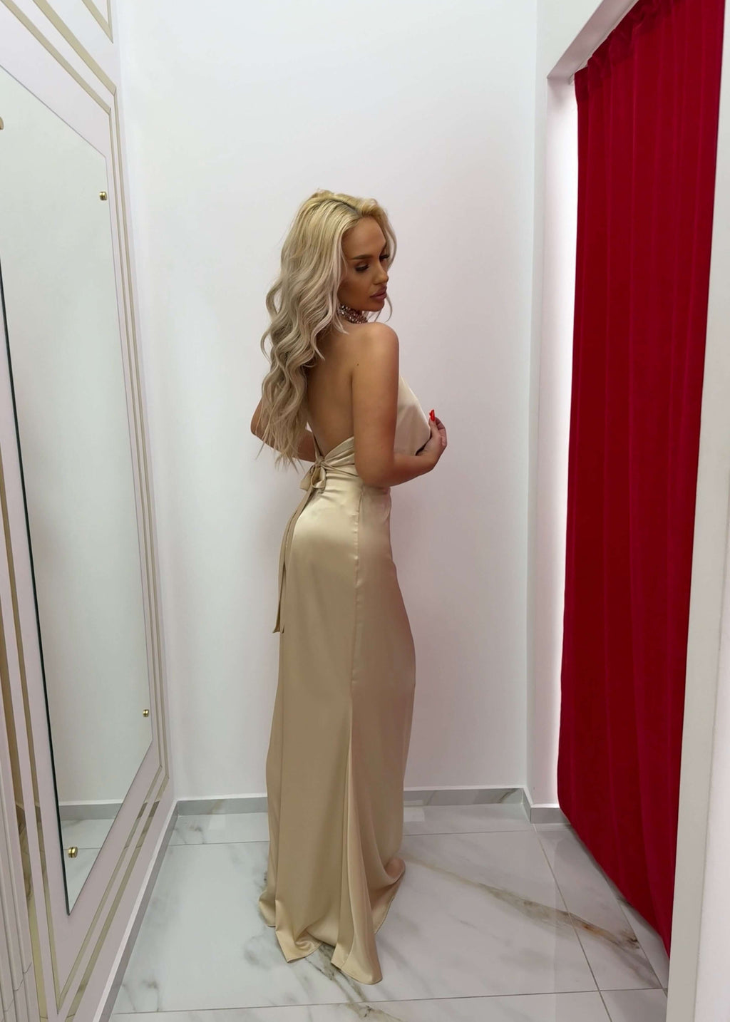 Rochie Bling Enchant din satin matase elastic, lunga cu spatele gol, prezentata pe model blond in cabina de proba eleganta