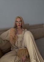 Compleu Bling Miray elegant din lycra cu cristale, bustieră, pantaloni evazați și mantou cu pene, purtat pe canapea bej