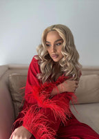 Compleu roșu elegant cu pene, model așezat pe canapea, look glam pentru seară și evenimente speciale